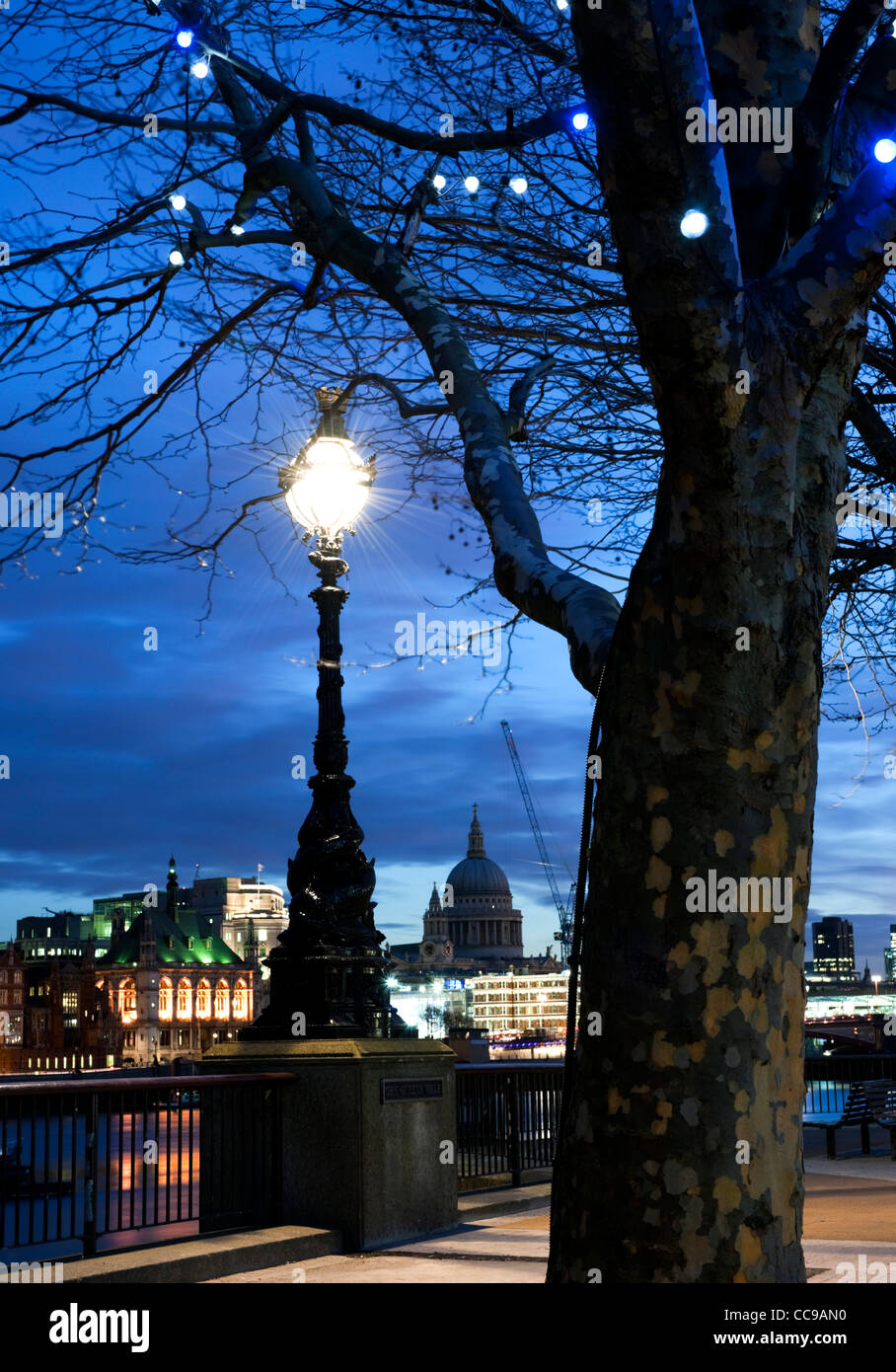 Queen's Walk, South Bank di Londra SE 1 con banchi vuoti e l'illuminazione di una strada con lo skyline della città tra cui la Cattedrale di St Paul Foto Stock
