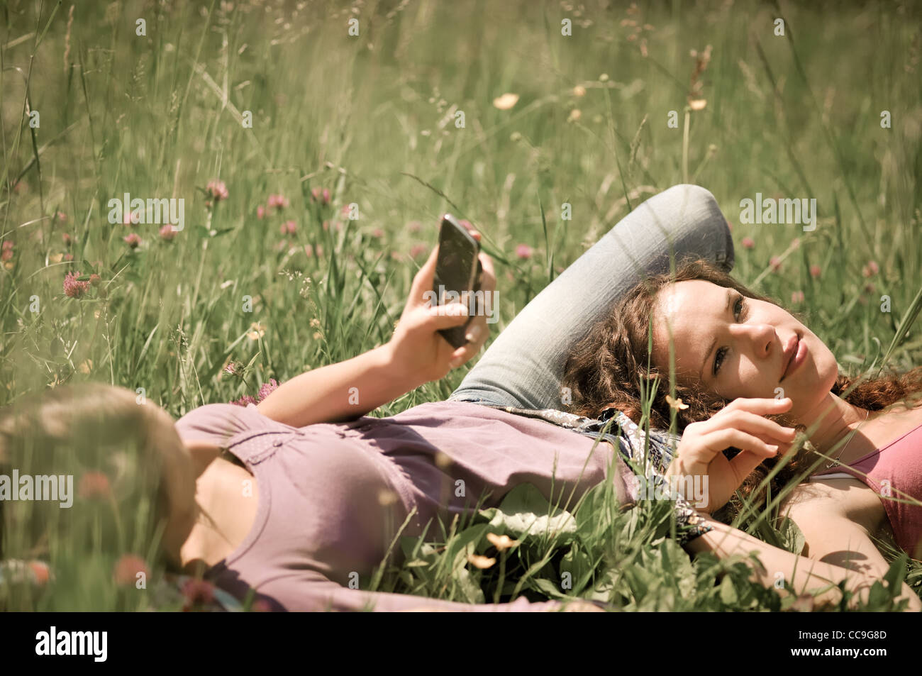 Due amici (ragazze adolescenti) relax sdraiati sull'erba al di fuori nella natura - una ragazza è tramite cellulare Foto Stock