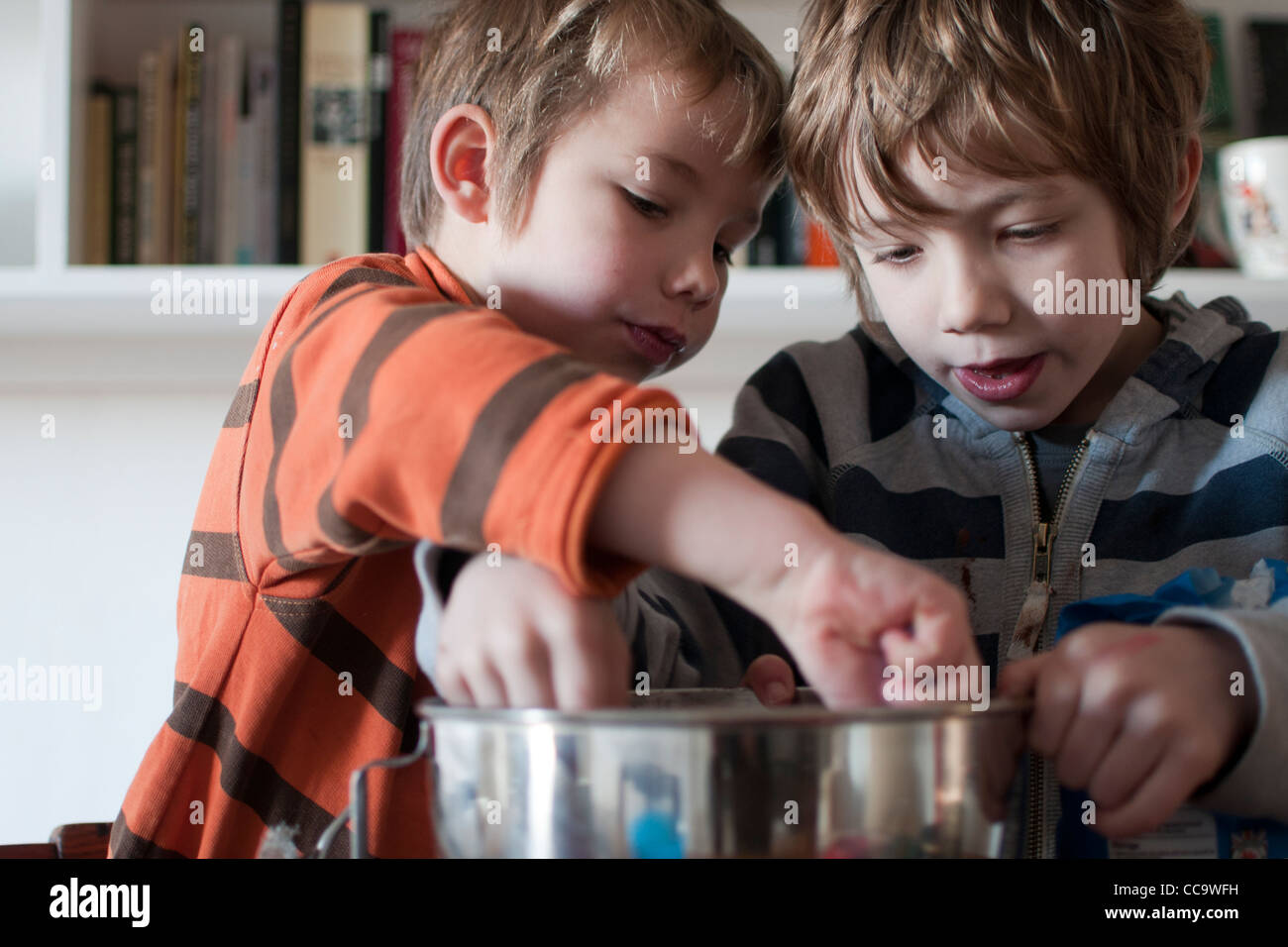 Due giovani ragazzi la cottura di una torta al cioccolato - leccare la miscela per torte al di fuori del recipiente Foto Stock