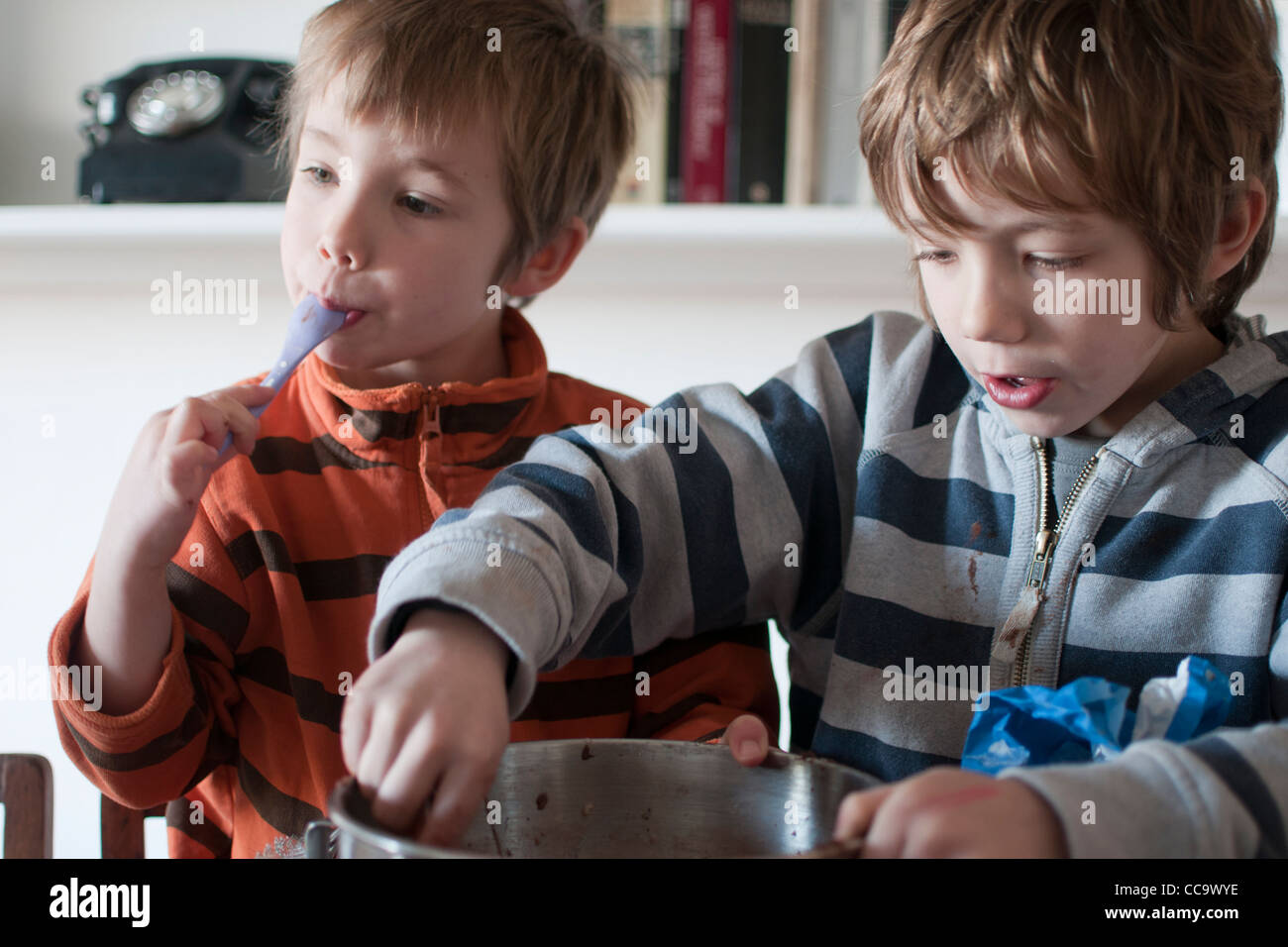 Due giovani ragazzi la cottura di una torta al cioccolato - leccare la miscela per torte al di fuori del recipiente Foto Stock