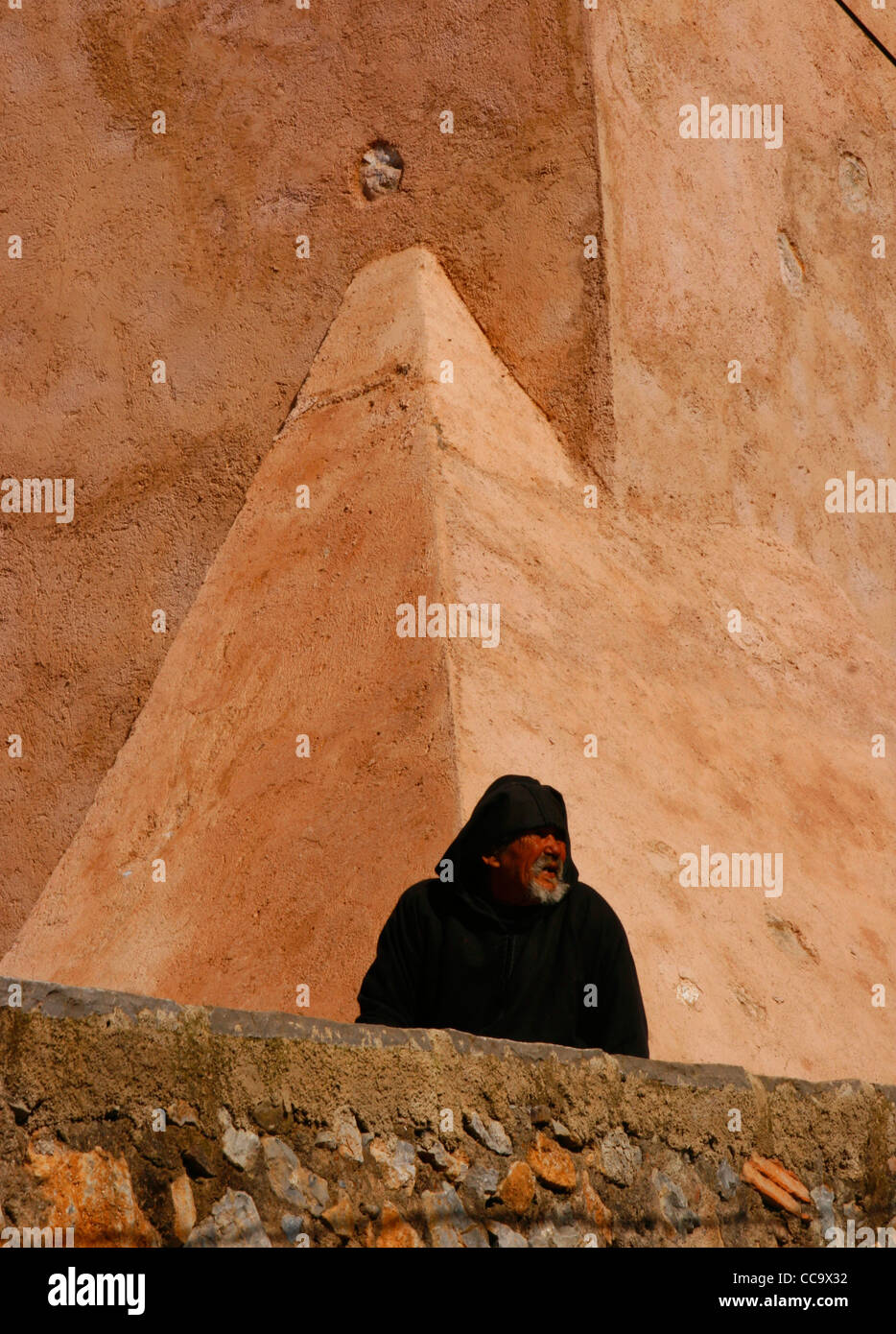 Un anziano che indossa un djellaba tradizionale con il Chefchaouen la parete in background. Il Marocco. Foto Stock