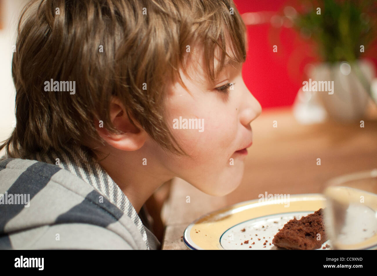 Felice giovane ragazzo seduto a tavola a mangiare un pezzo di cioccolato pan di spagna Foto Stock
