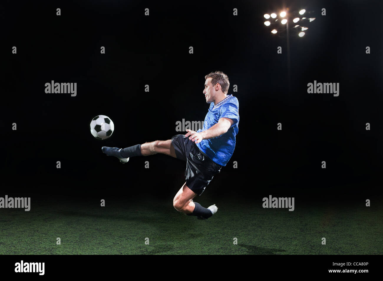 Giovane giocatore di calcio salta in aria a calciare la sfera Foto Stock