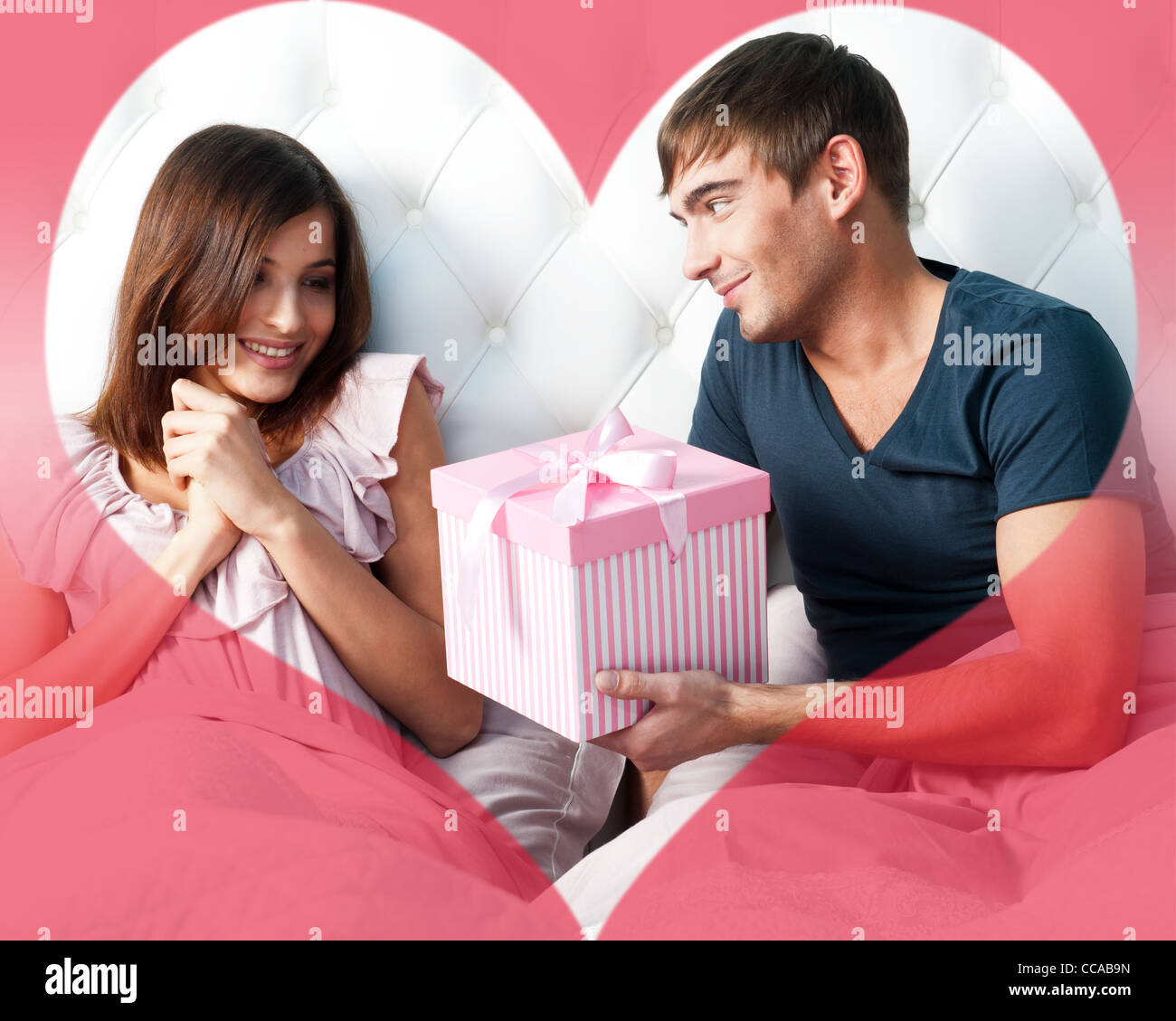 Closeup Ritratto di una felice coppia giovane rilassante sul letto. Uomo che fa un regalo alla sua ragazza. Il giorno di San Valentino Foto Stock