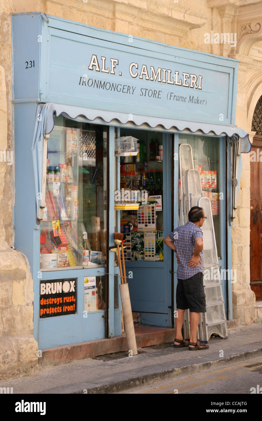 Proprietario in piedi al di fuori del suo negozio di ferramenta nella strada laterale a La Valletta. Foto Stock