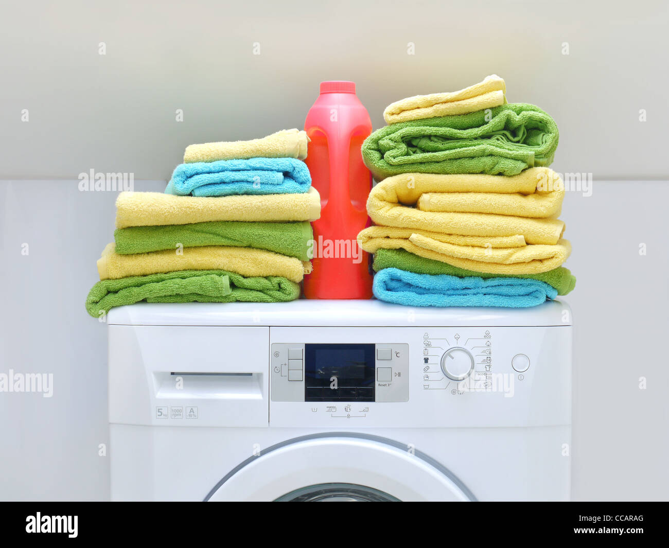 Pila di freschi asciugamani colorati e una bottiglia di detergente sulla macchina di lavaggio Foto Stock