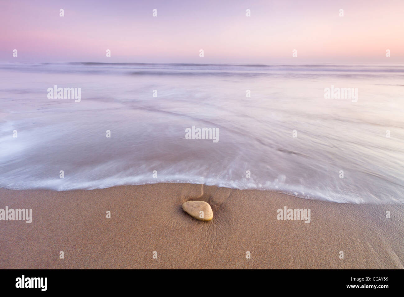 Lavaggio in acqua su una pietra sulla spiaggia di Druridge Bay nei pressi di Ellington, Northumberland, Inghilterra Foto Stock