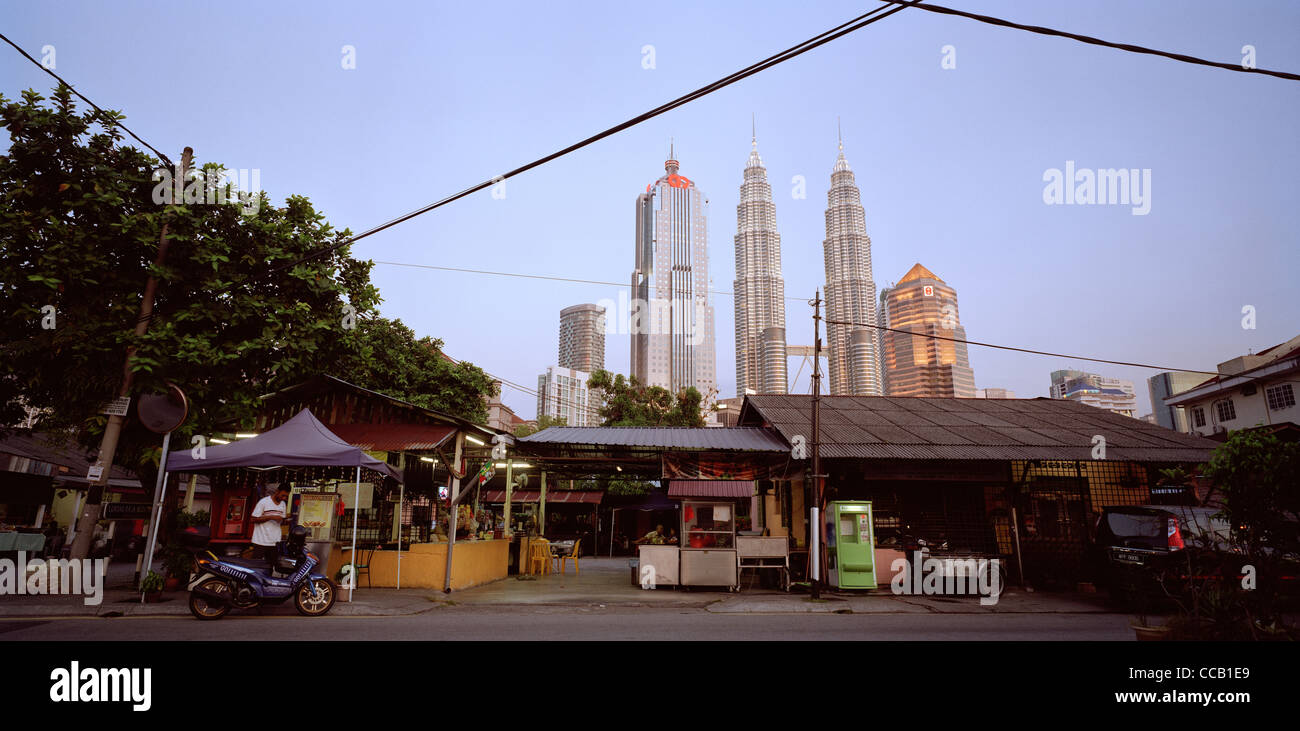 Il tramonto e la notte scende come le Torri Petronas incombono su di Kampung Baru nella città di Kuala Lumpur in Malesia in Estremo Oriente Asia sud-orientale. Città Travel Foto Stock