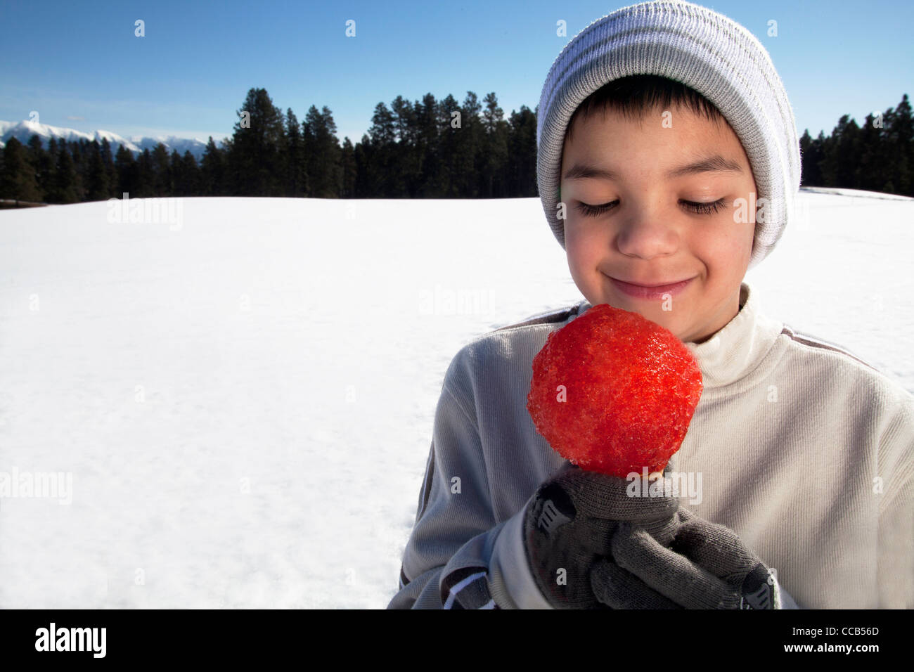 Ragazzo 10 -12 anni di mangiare un cono di neve su una giornata invernale all'esterno. Foto Stock
