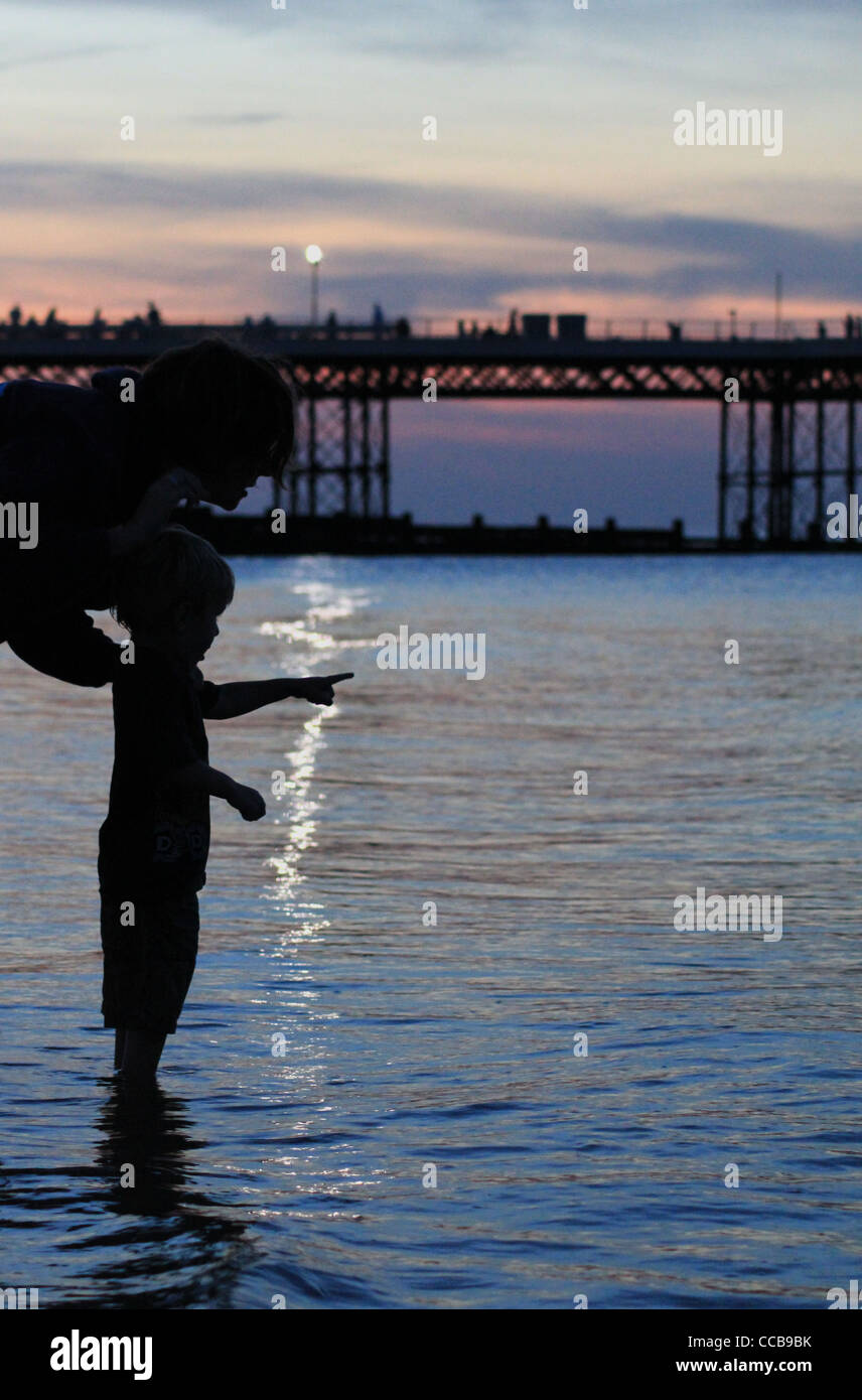 Un giovane ragazzo ricorda al mare, stagliano dal sole di sera, mentre la remata con sua madre. Foto Stock