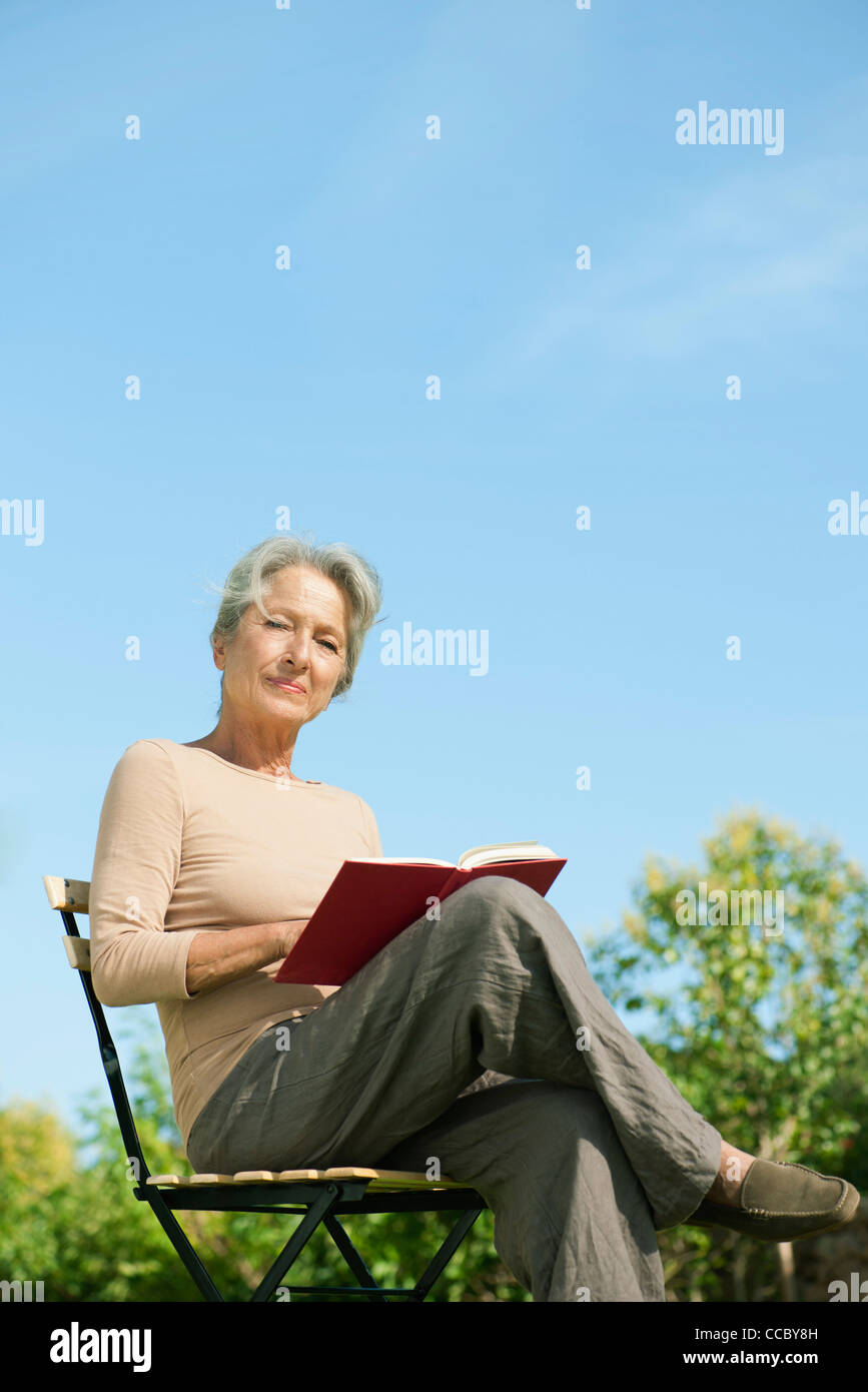 Senior donna seduta all'aperto con Libro, ritratto Foto Stock