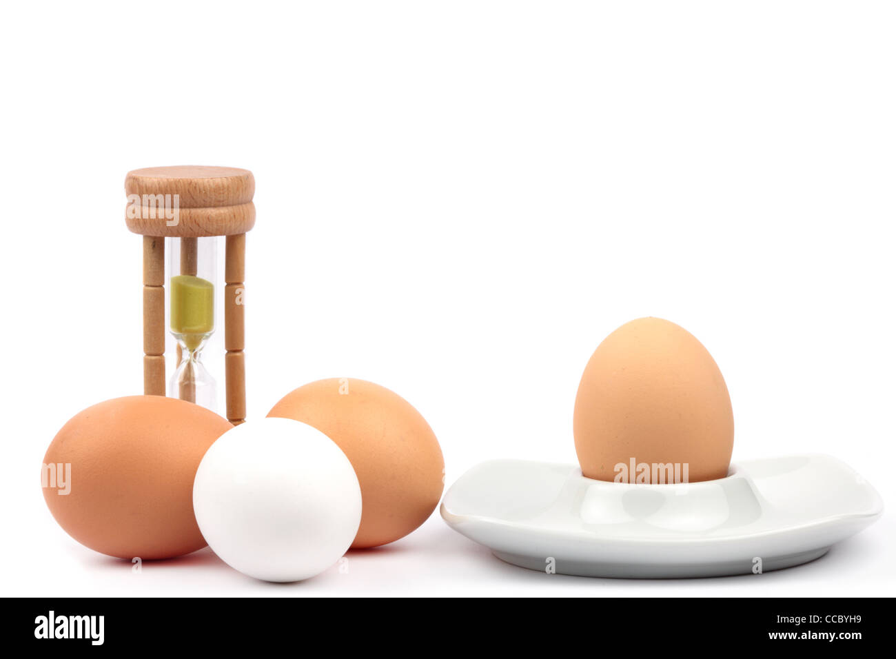 Uova di gallina e tazze di uovo e timer di uovo di fronte a uno sfondo bianco Foto Stock