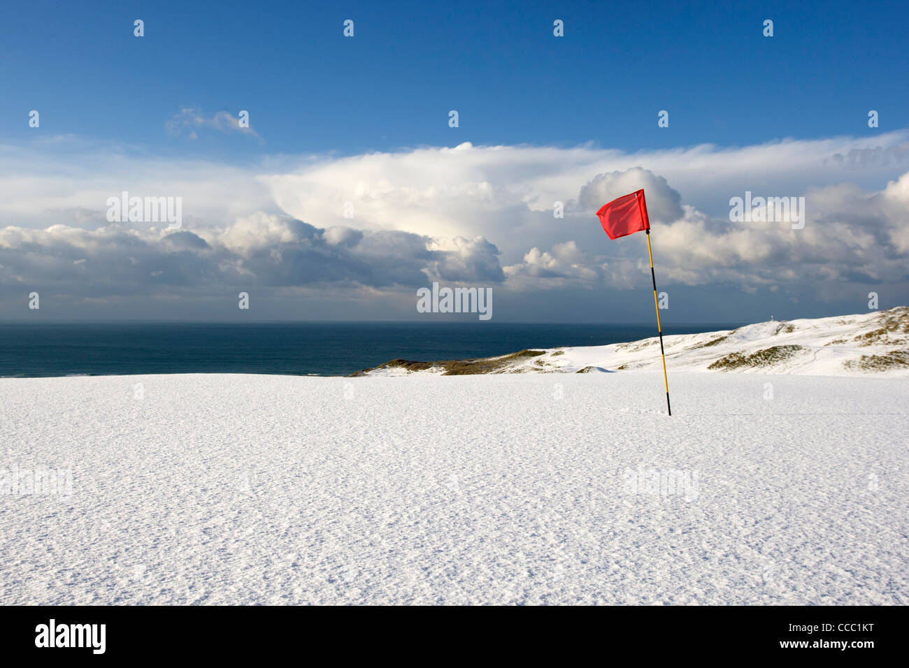Una bandiera rossa sorge nella neve su uno dei verdi presso il campo da golf a Perranporth Cornwall. Foto Stock