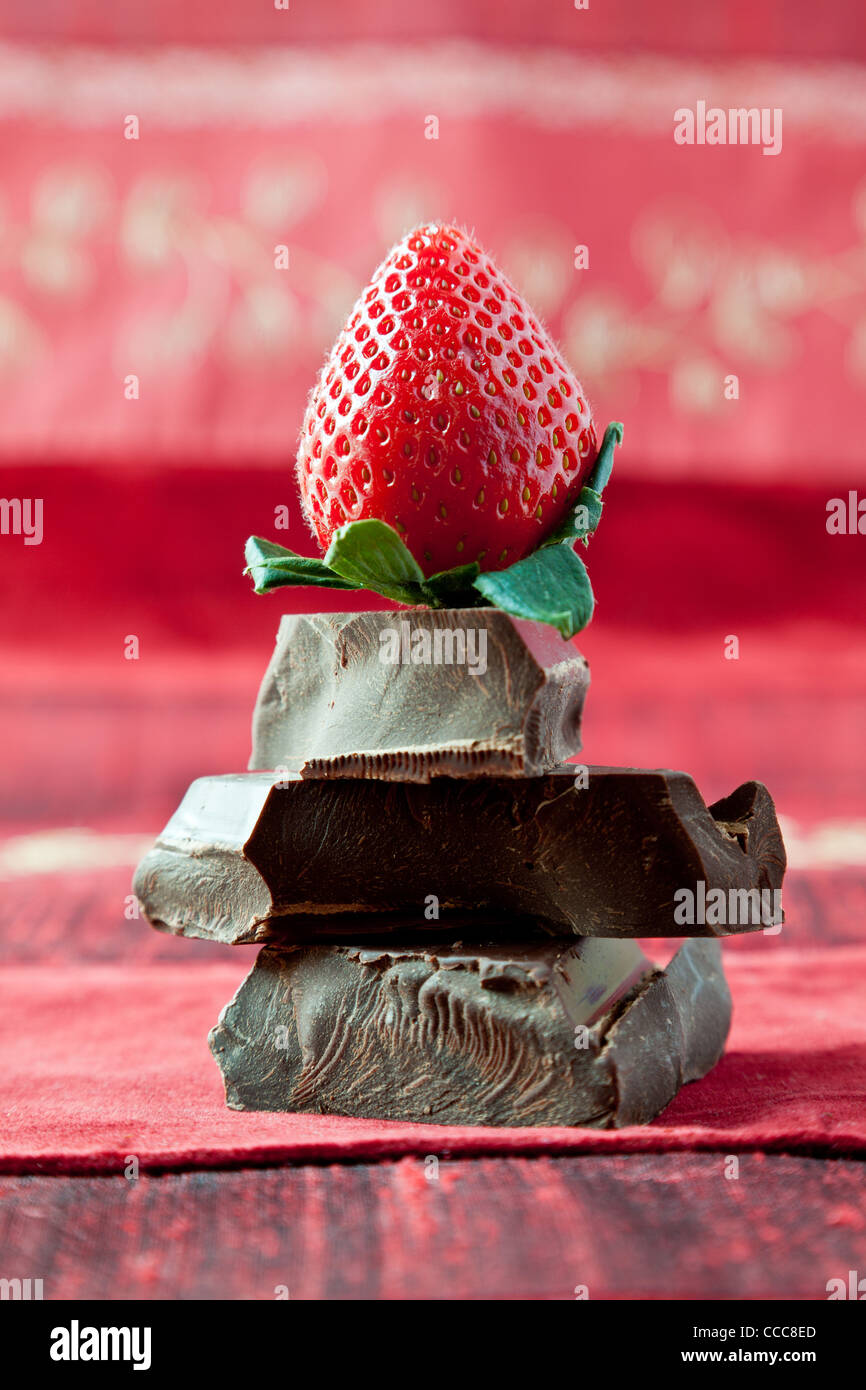 Fragola sulla parte superiore della pila di spessore gourmet dark chocolate bar chunk. Rosso sfondo a trama. Foto Stock