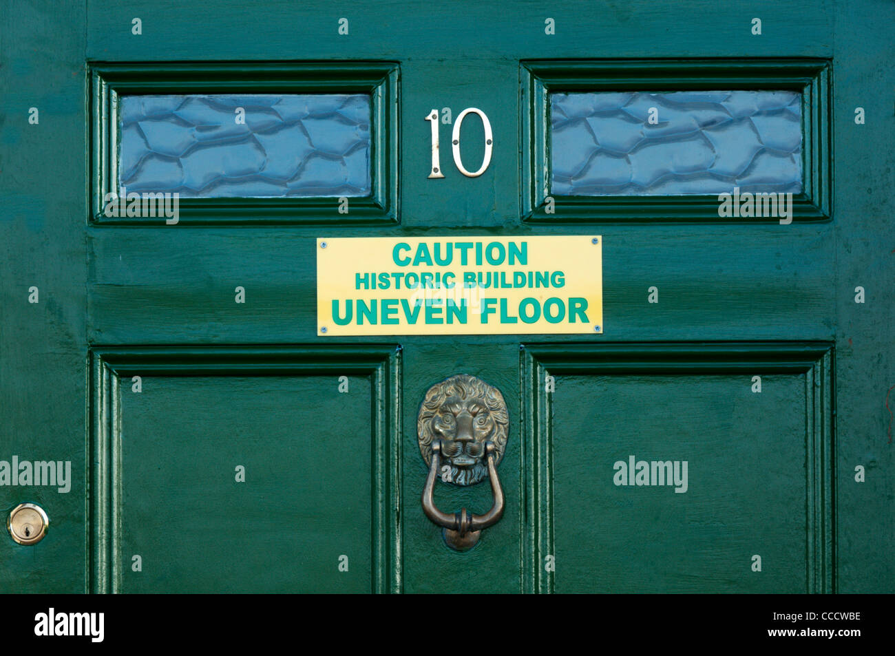 Segno su una porta verde avverte in caso di pavimenti irregolari in un vecchio edificio. Foto Stock