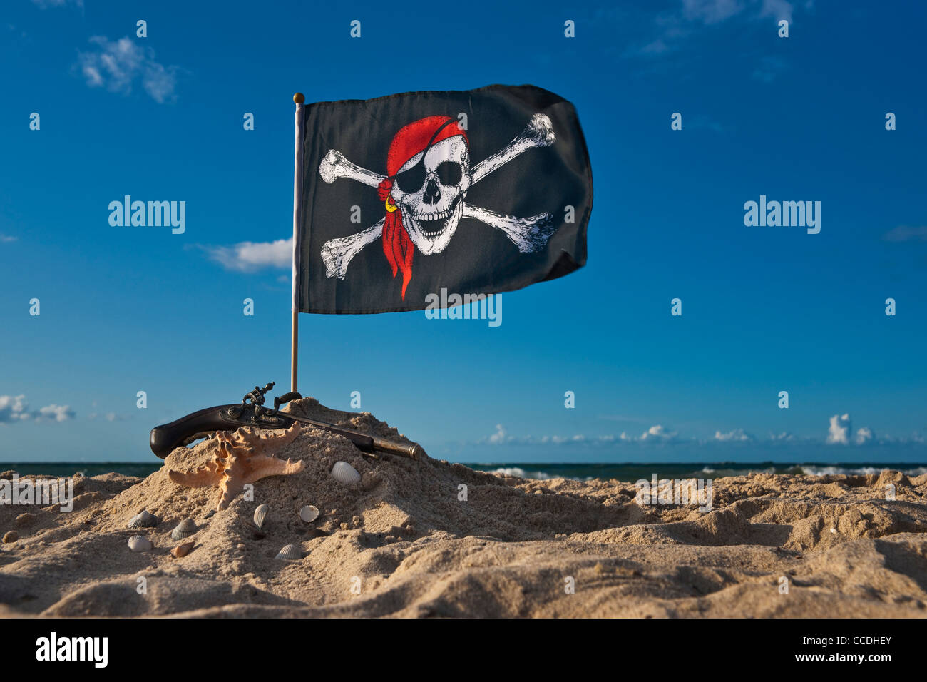 Un pirata bandiera soffia sulla spiaggia, a fianco è una pistola e una stella di mare Foto Stock
