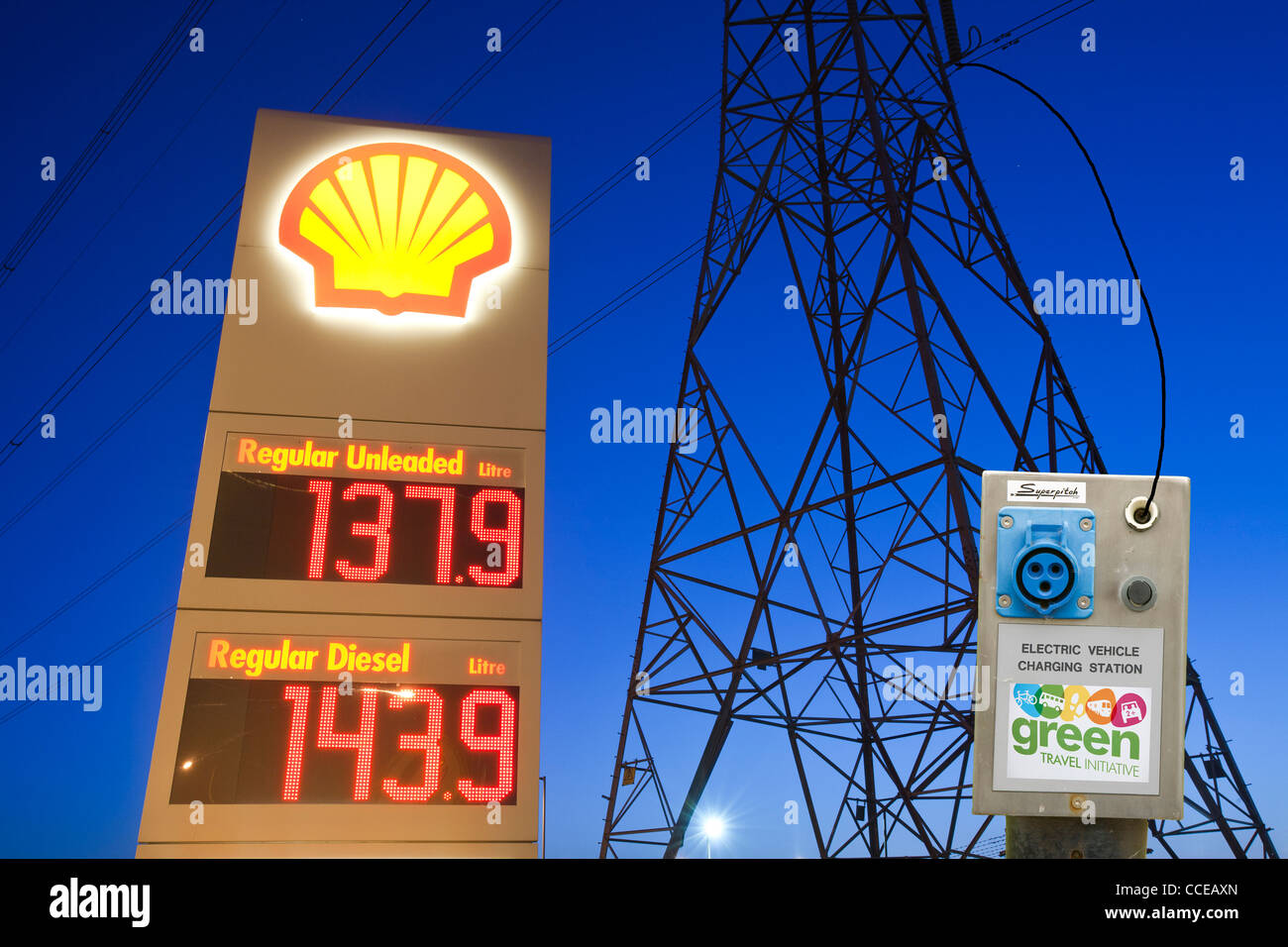 Una benzina sation in Billingham su Teeside, Regno Unito, con un traliccio di elettricità al tramonto e un auto elettrica stazione di ricarica. Foto Stock