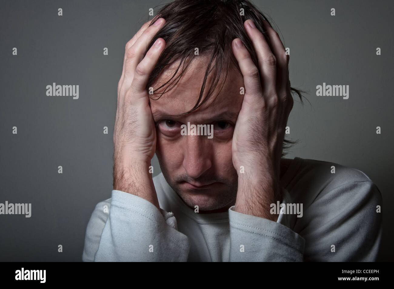 Molto deprimente Uomo in camicia bianca tenendo la testa con le mani in una luce bassa atmosfera. Foto Stock