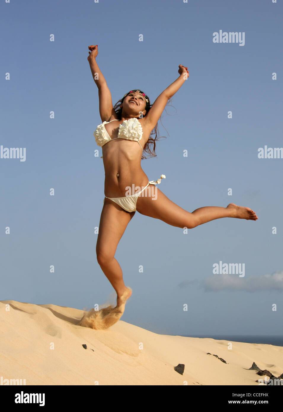 Ragazza indonesiana in una crema Bikini salti di gioia sulle dune di sabbia di Corellejo Riserva Naturale, Fuerteventura, Isole Canarie. Foto Stock