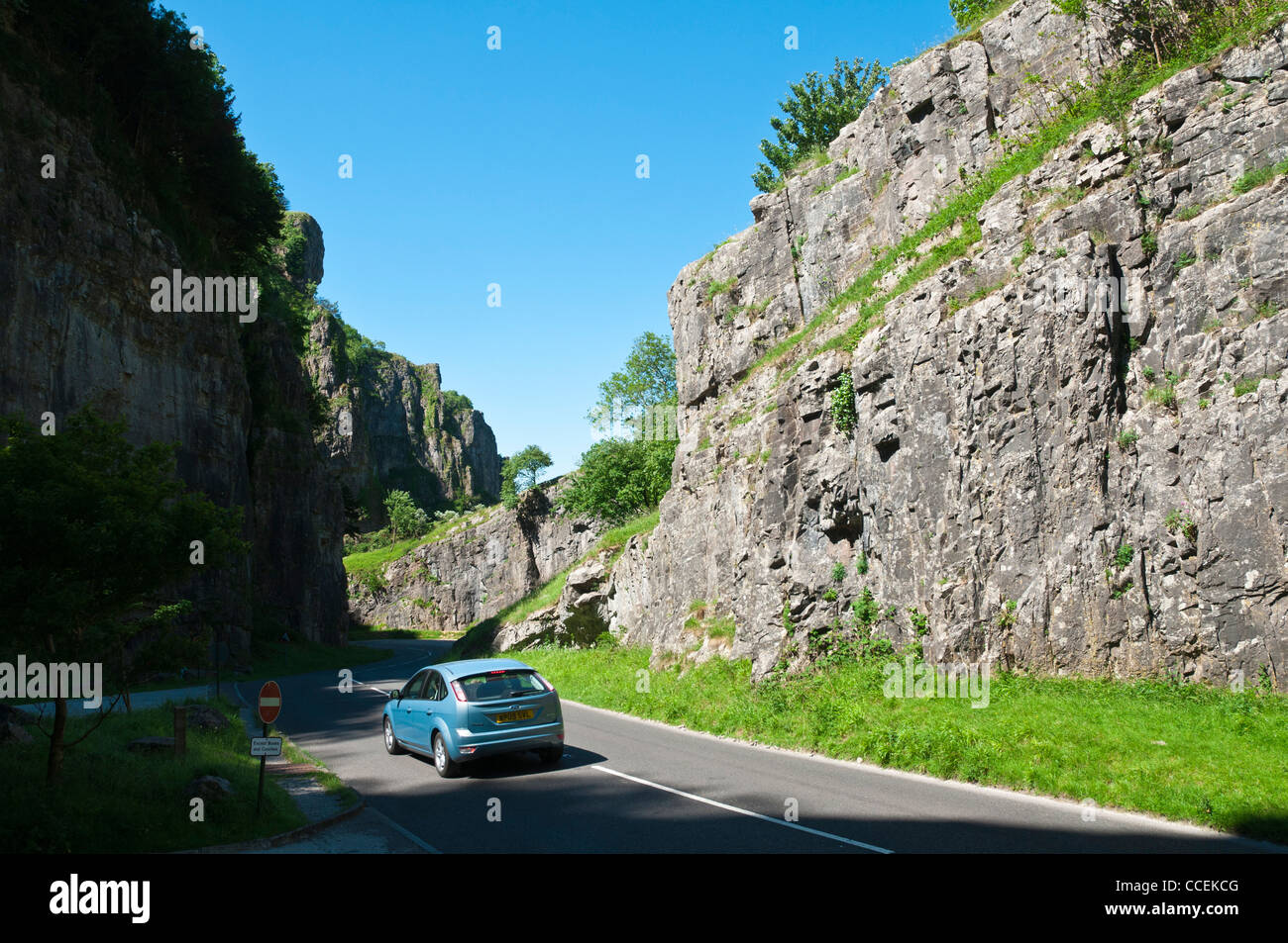 Una soleggiata giornata estiva nel mondo famoso Cheddar Gorge nel Somerset con un auto blu guidando lungo la strada Foto Stock
