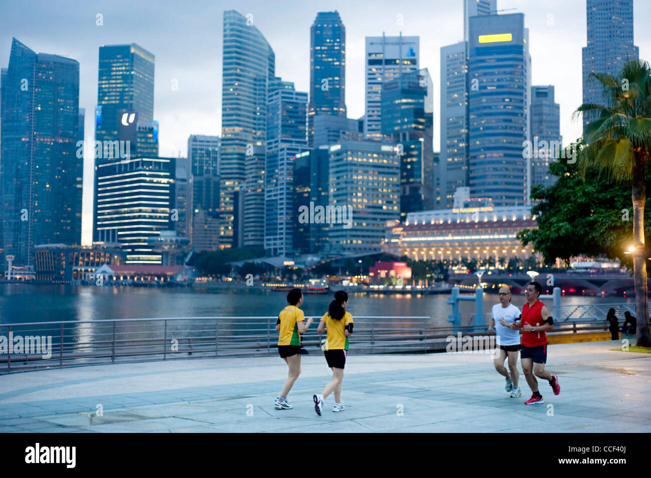 Le persone che eseguono la sera sul terrapieno nella parte anteriore del centro business. In esecuzione è molto sport popolari in Singapore Foto Stock