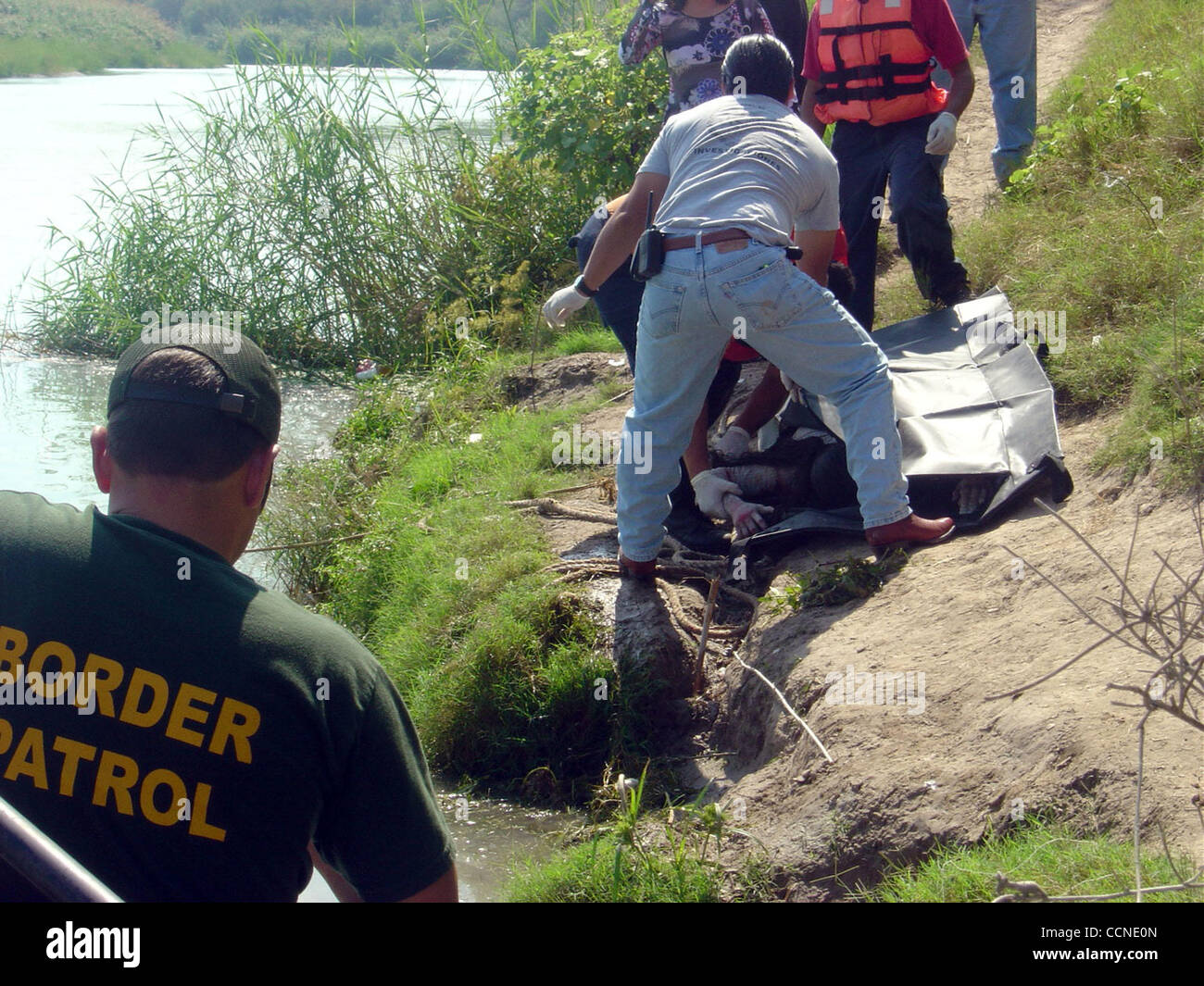 Un immigrato messicano, trovato morto nel Rio Grande del sabato mattina a poche miglia a sud di Campeche, Messico, la città di confine di fronte a Eagle pass, è messo su un nero tarp dalle autorità messicane, come un U.S. Pattuglia di Confine agenti guardare da una barca. La donna muore affogato nel fiume con la figlia Foto Stock