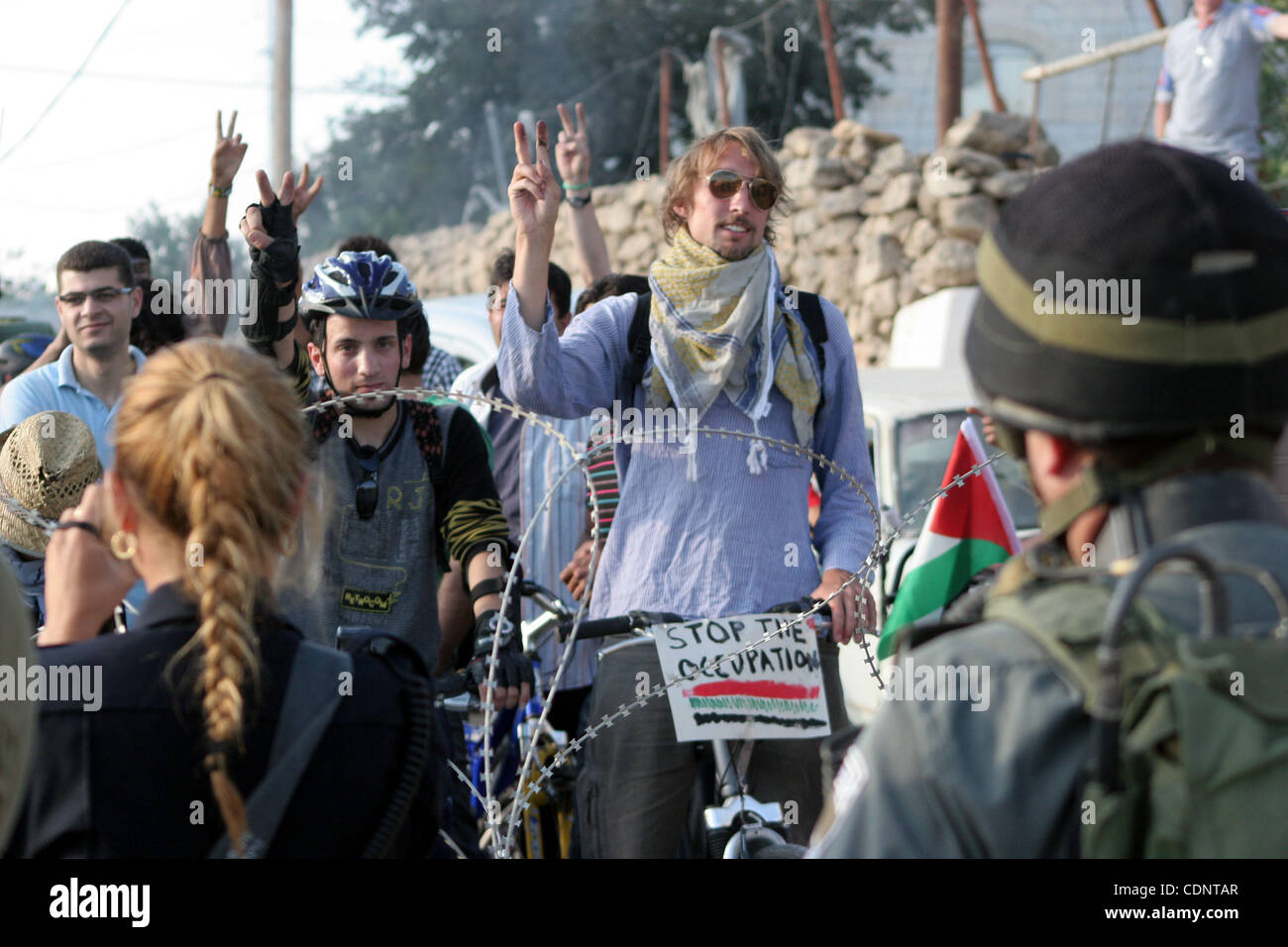 Palestinesi e stranieri bikers attendere dietro il filo spinato e un cordone di forze di sicurezza israeliane di cavalcare le loro biciclette sotto lo slogan di "mountain bike senza frontiere' attraverso una strada palestinese chiuso da truppe israeliane per essere utilizzato dai coloni ebrei che vivono nella città di Hebron in Cisgiordania occupata il 2 giugno Foto Stock