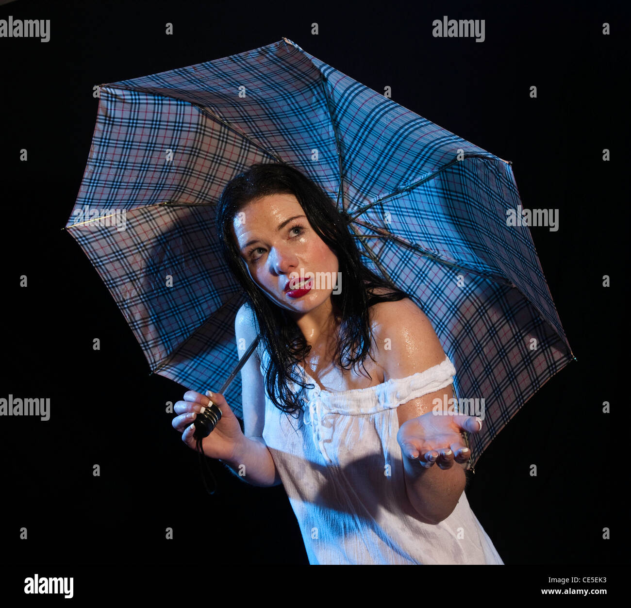 Attraente giovane donna si ripara dalla pioggia sotto un ombrello Foto Stock
