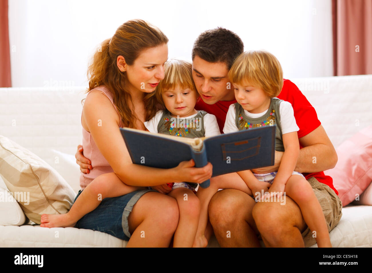Il padre e la madre in cerca album di foto con i gemelli figlie Foto Stock