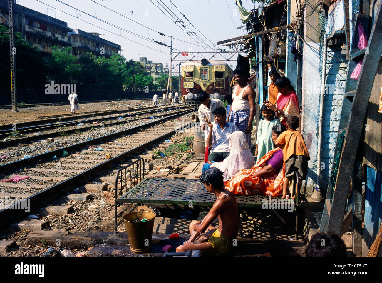 Le persone che soggiornano boy la balneazione donna seduta sul letto di metallo in baraccopoli vicino al binario ferroviario Harbor line bombay Mumbai India Maharashtra Foto Stock