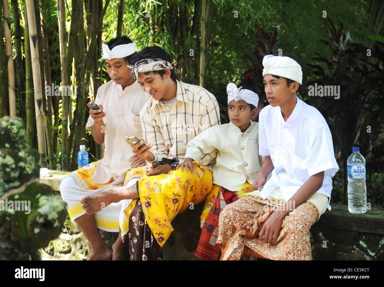 Famiglia tradizionale cerimonia di guardare quando si utilizzano telefoni cellulari in Bali Orientale, Indonesia Foto Stock