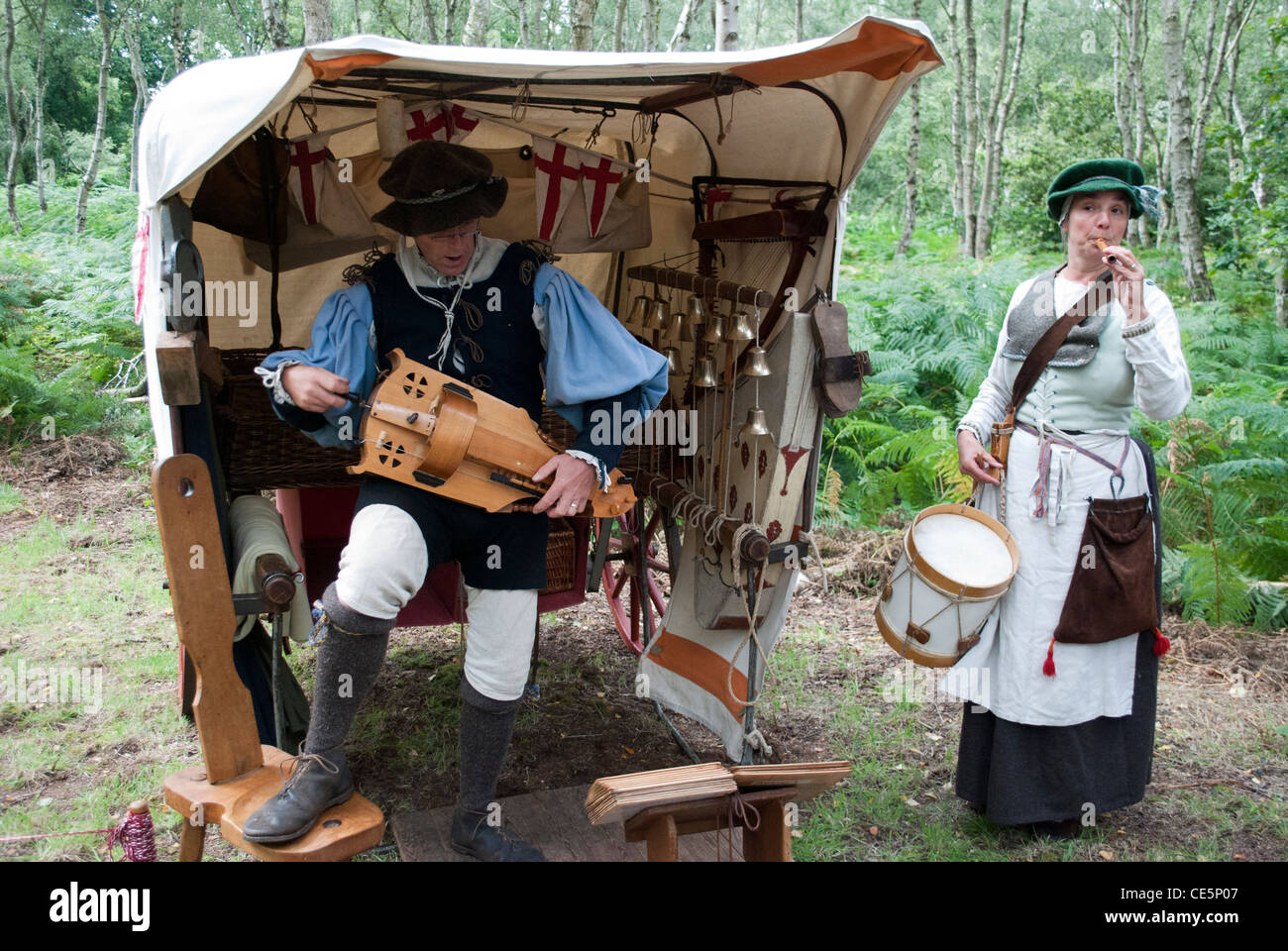 L uomo e la donna vestita come musicisti medievale di fronte ad una tenda e alberi giocando organetto di Barberia, il tamburo e il registratore Foto Stock