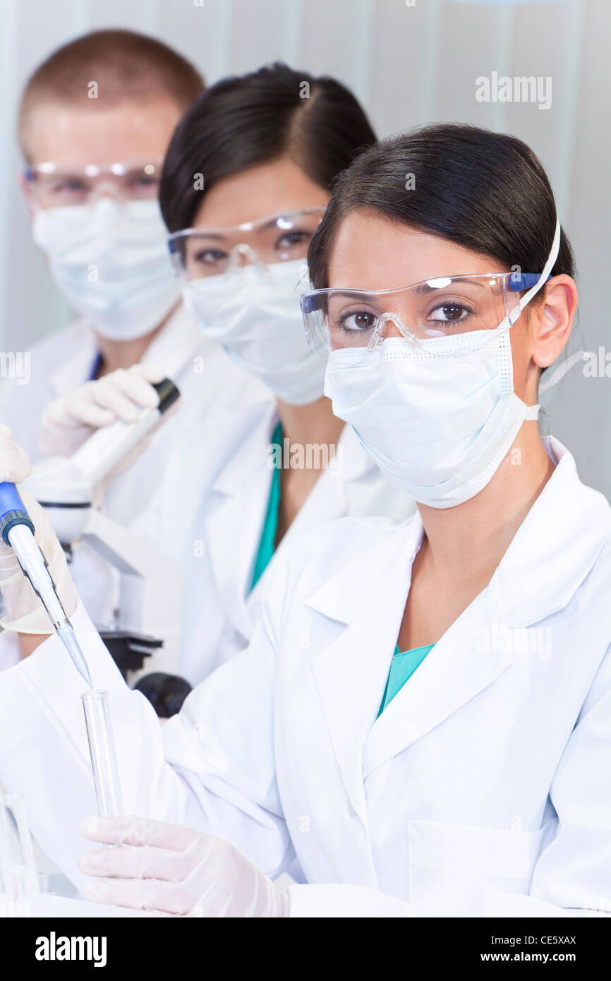 Una femmina di medici o di ricercatore scientifico o medico usando una pipetta e provetta di liquido chiaro in un laboratorio con il suo team Foto Stock
