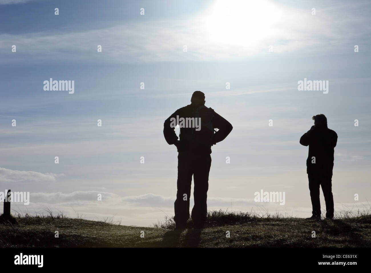 Silhouette di due uomini guardando la vista dalla cima di una collina retroilluminati da sun. Newborough Warren, Isola di Anglesey, Galles del Nord, Regno Unito. Foto Stock