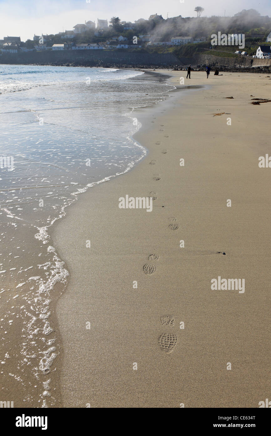 Coverack, Cornwall, Inghilterra, Regno Unito. Spiaggia tranquilla con impronte lungo il litorale e la nebbia al di sopra del villaggio Foto Stock