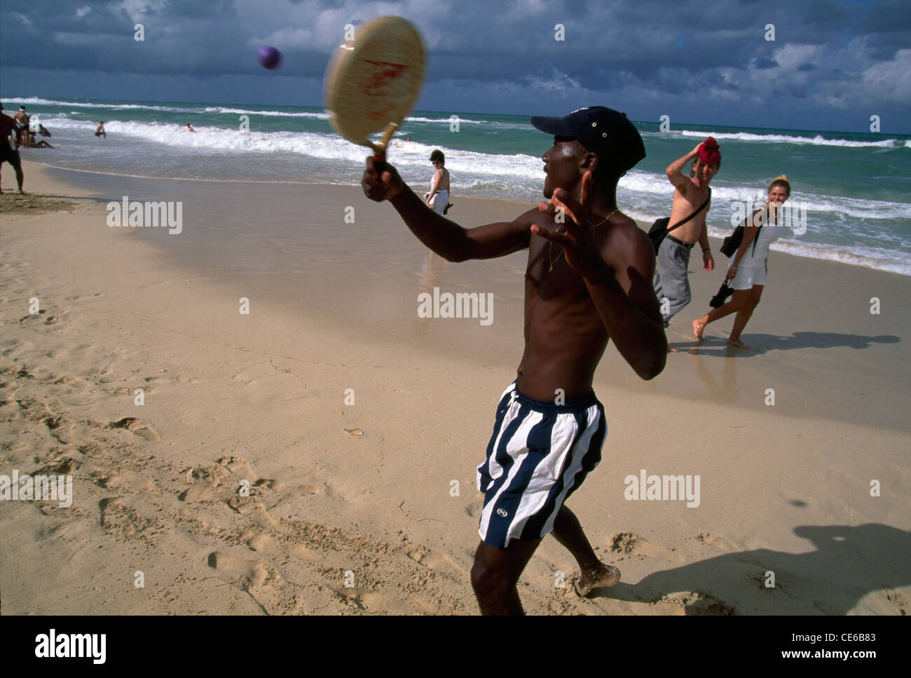 I turisti stranieri a piedi sulla spiaggia mentre la gente cubana giocare racket ball alla spiaggia di Santa Maria, Cuba. Foto Stock