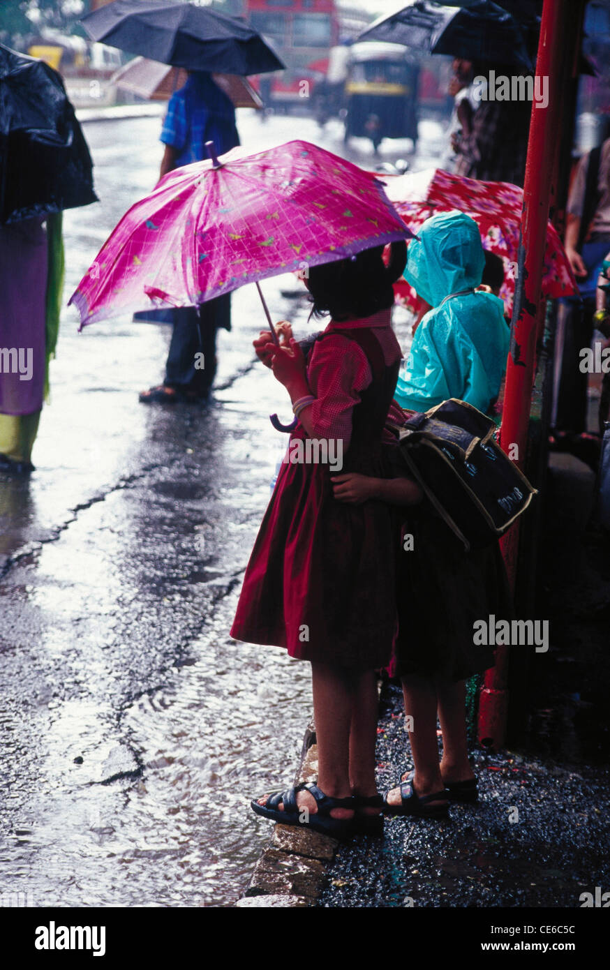Andando a scuola i bambini ombrelli azienda in piedi alla fermata bus sulla strada in piogge monsoniche ; Mumbai Bombay ; maharashtra ; india Foto Stock