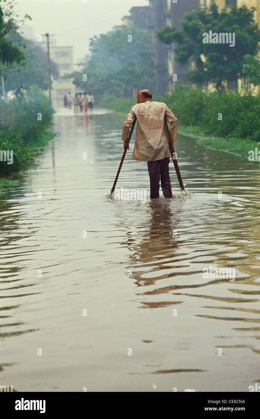 Uomo con le stampelle a piedi in caso di esondazione sulla strada dopo il monsone di Bombay Mumbai India Maharashtra Foto Stock