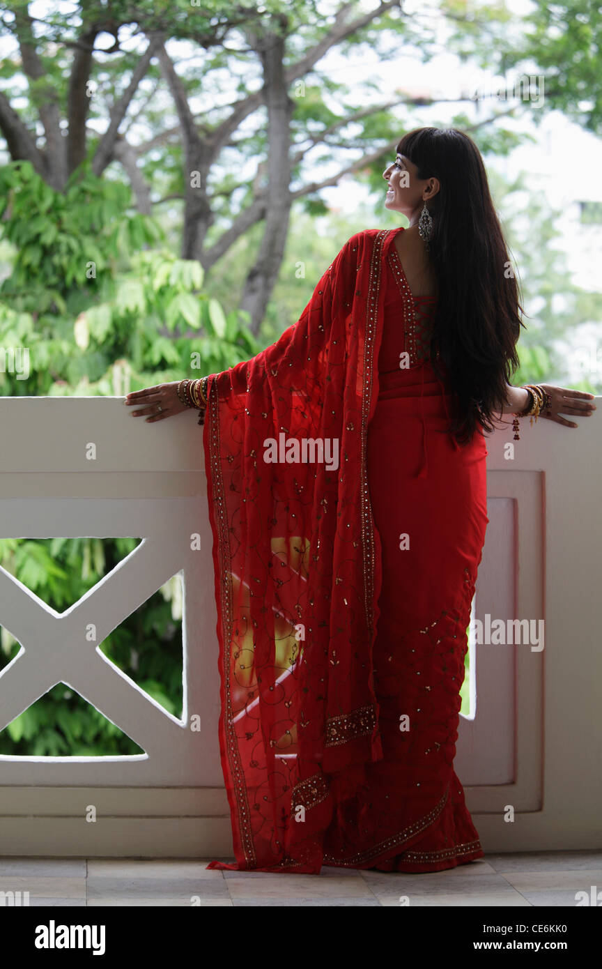 Torna shot indiana di donna che indossa un sari rosso che si affaccia su un balcone. Foto Stock