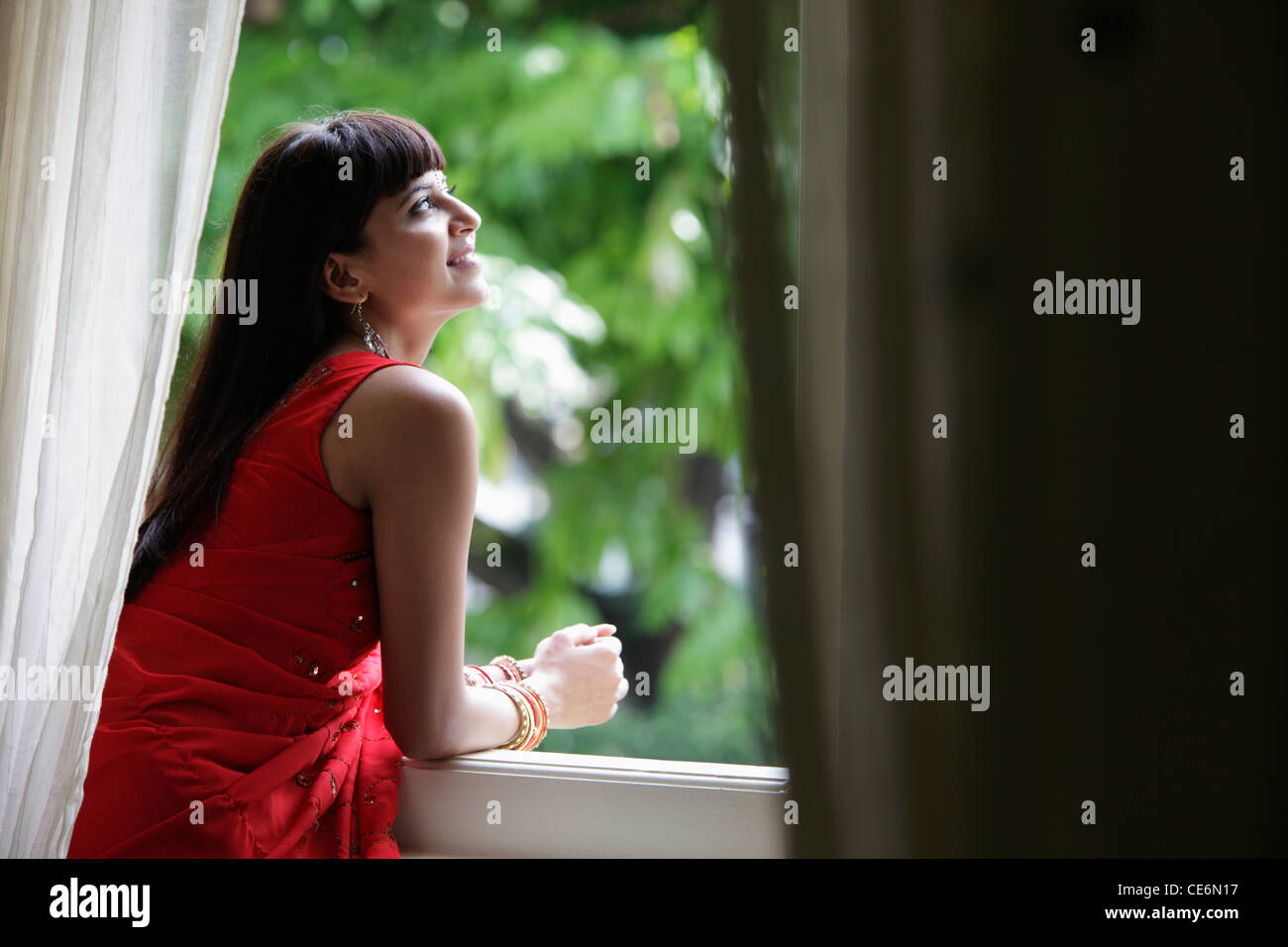 Donna indiana a guardare fuori dalla finestra, sorridente Foto Stock