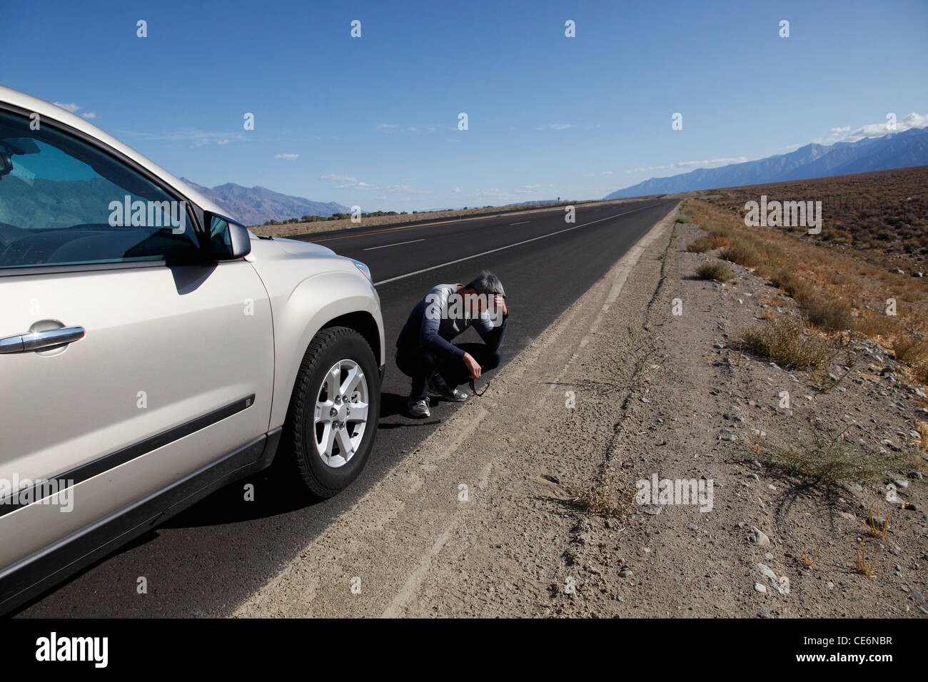 L'uomo accovacciato in basso sul lato della strada dalla sua vettura con la testa in giù Foto Stock
