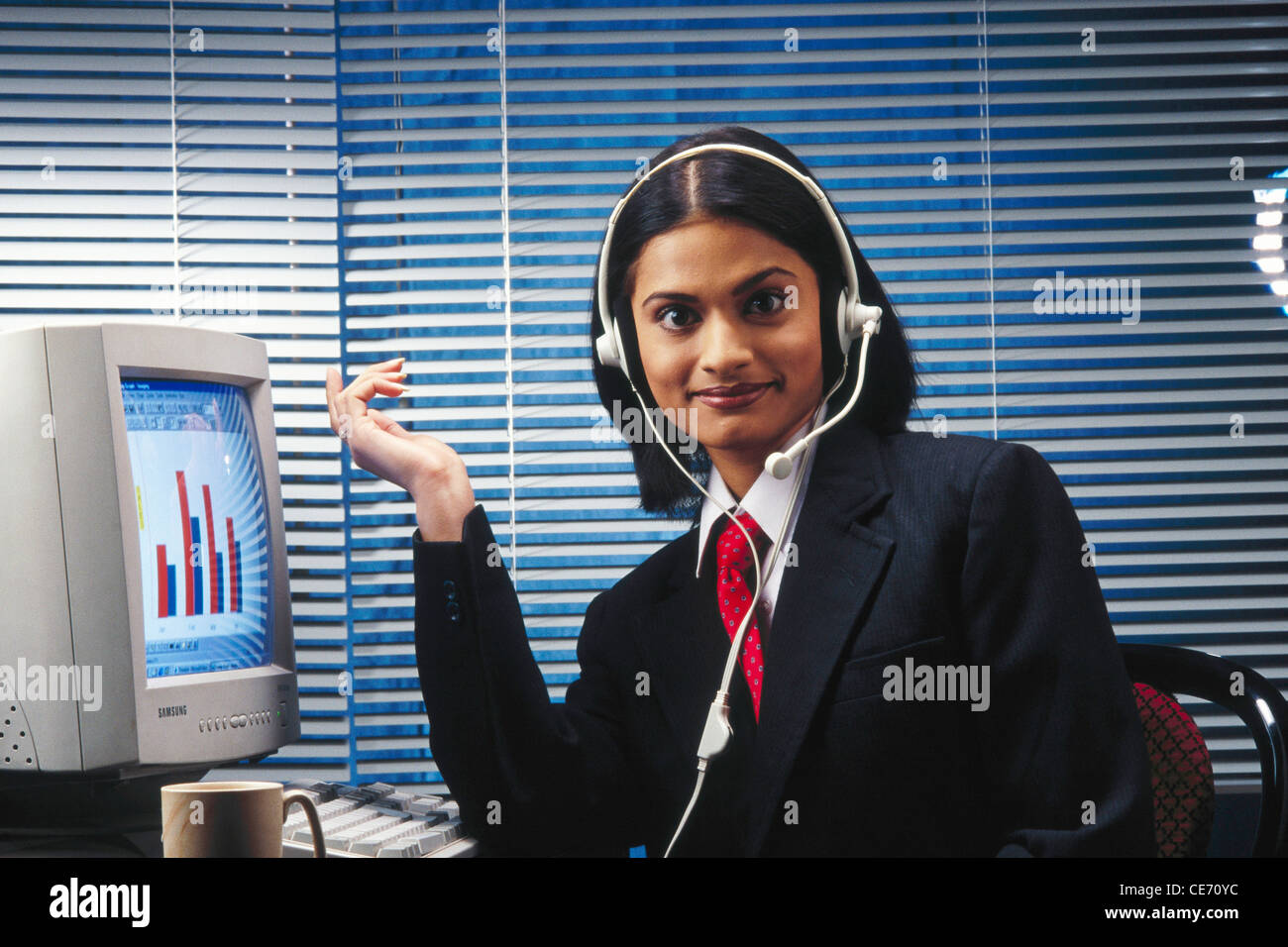Donna indiana con cuffie che lavora sul computer con giacca e cravatta guardando la fotocamera - modello release n. 286 Foto Stock