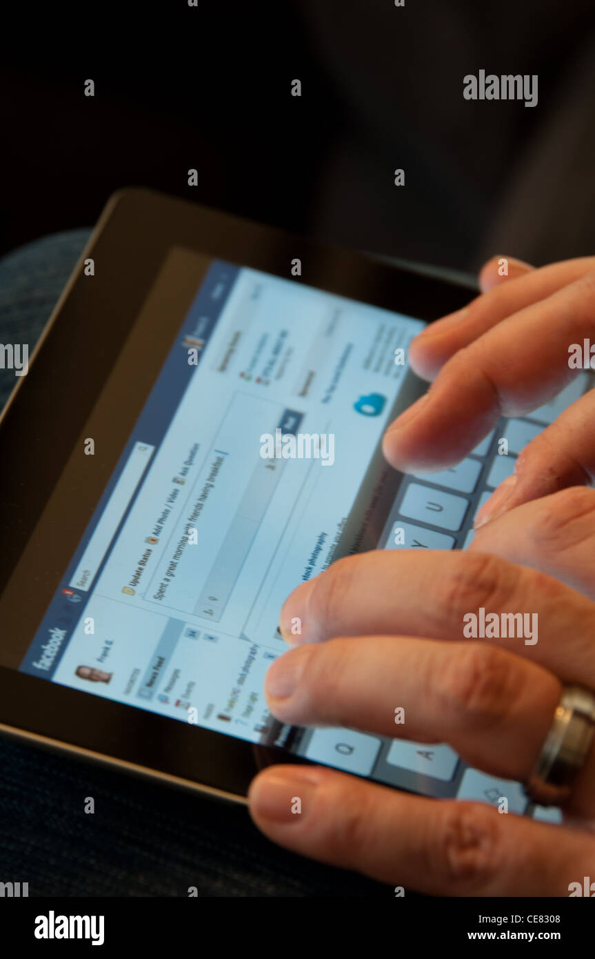 Close up di un iPad Apple schermata che mostra il sito web Facebook con due mani maschili la digitazione di un aggiornamento di stato Foto Stock