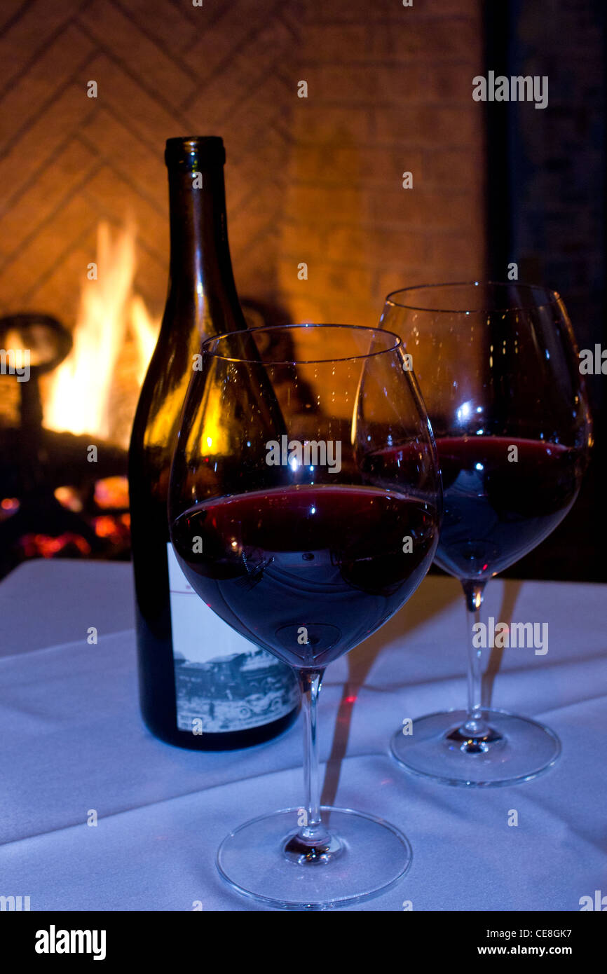 Due bicchieri di vino rosso e una bottiglia di vino di fronte al caminetto  Foto stock - Alamy