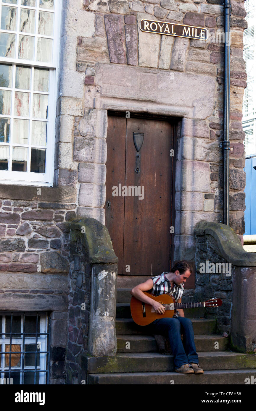 Edimburgo, Scozia, Regno Unito, Europa. Busker sat sui passi a suonare la chitarra sotto il royal Mile segno sopra Foto Stock