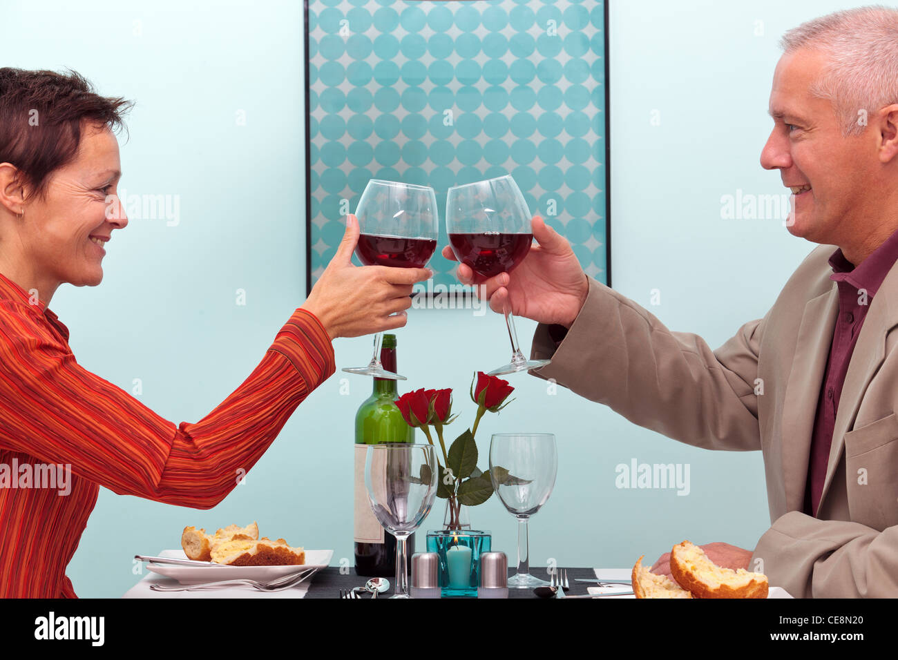 Foto di una coppia matura tostare i loro bicchieri di vino rosso mentre seduto in un ristorante Foto Stock