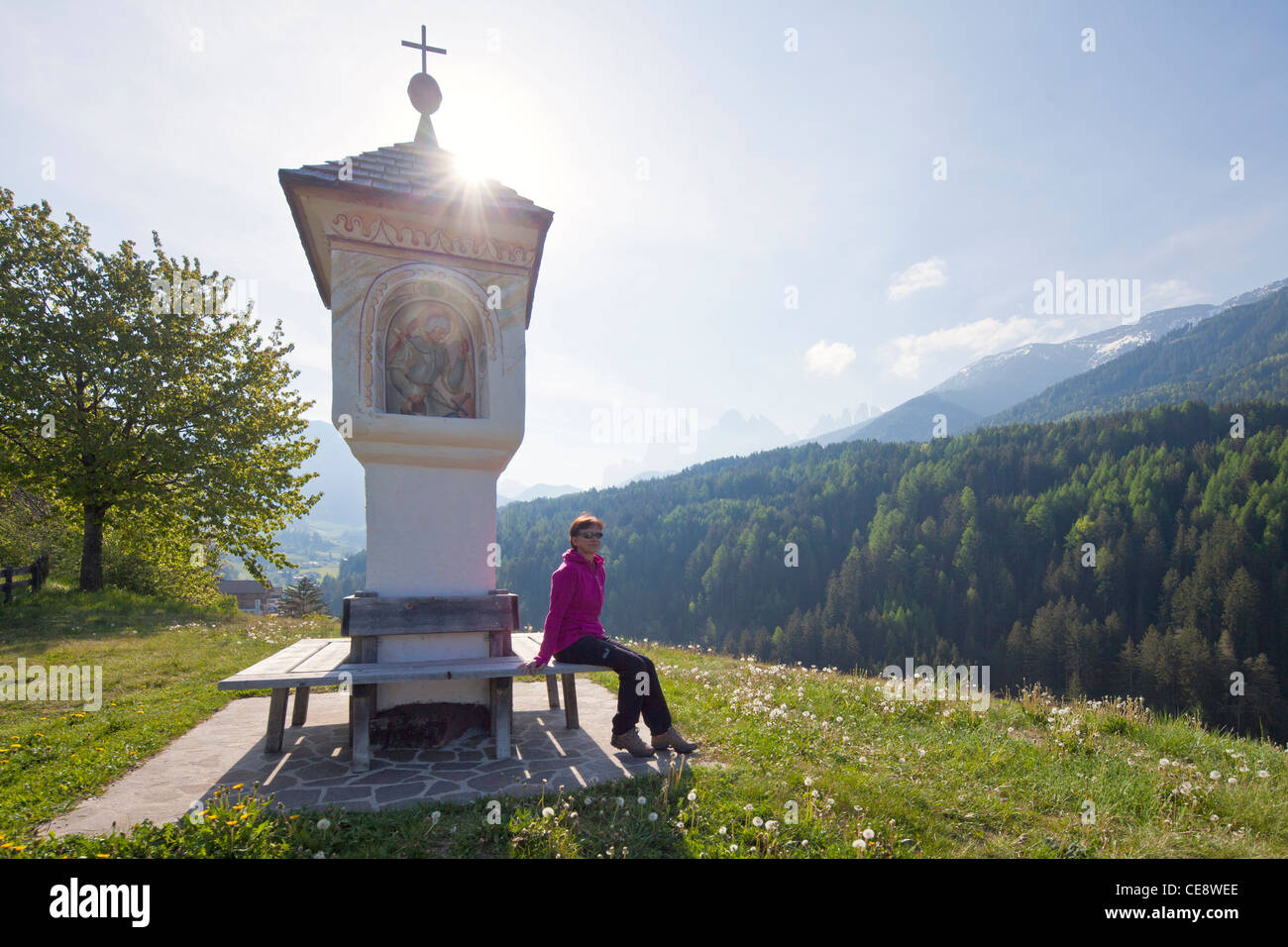 Donna seduta a una croce lungo il tragitto nella valle Villnoess, Dolomiti, Italia Foto Stock