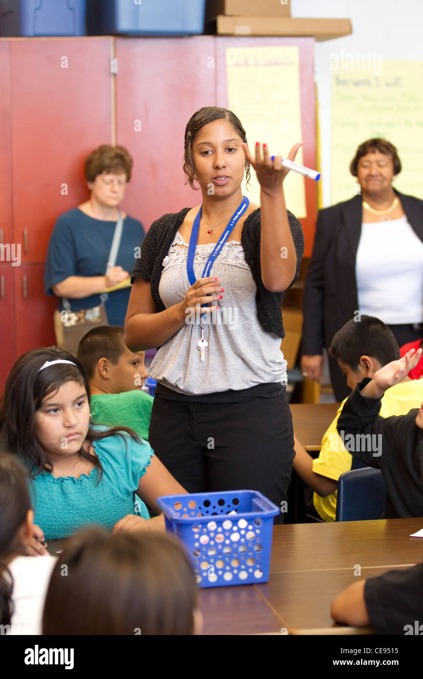 Giovane insegnante femmina incarica la scuola elementare di studenti di età come un gruppo di sostenitori di istruzione visitare la sua classe in Texas Foto Stock