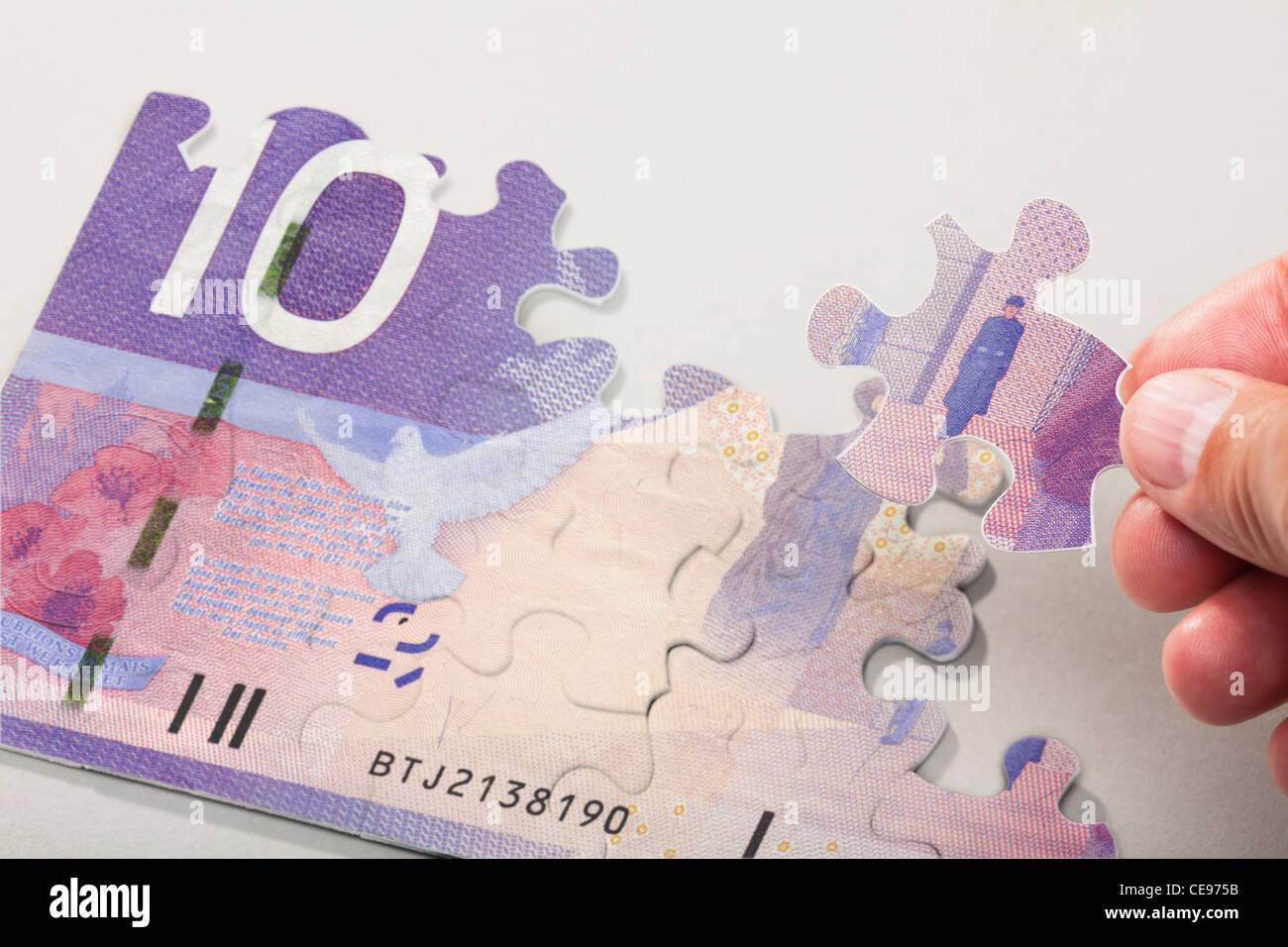 Maschio lato disponendo i pezzi del puzzle creazione di valuta canadese Foto Stock