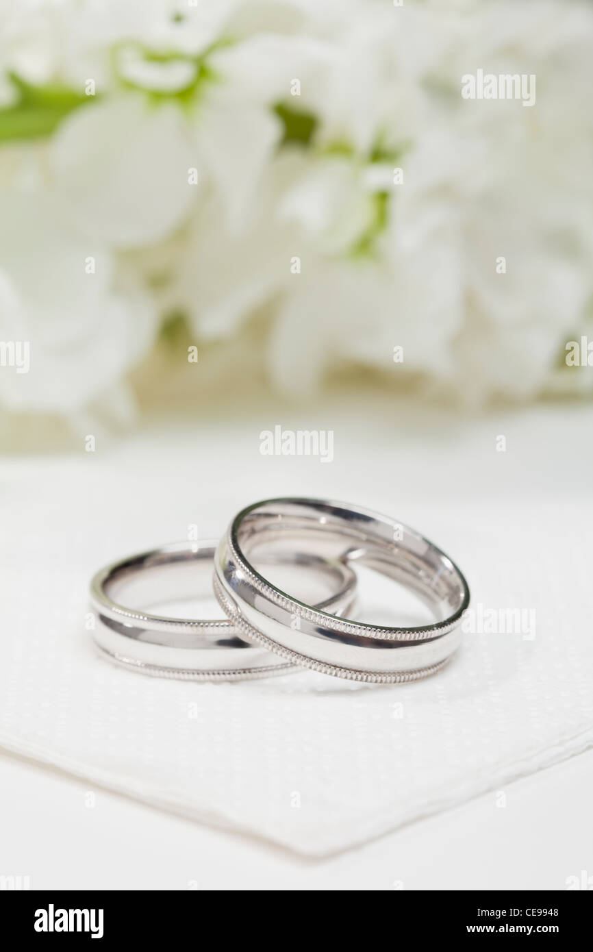 Close-up di anelli di nozze con fiori di colore bianco in background Foto Stock